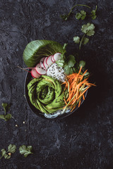 Obraz premium Raw vegan bowl with rice noodles, carrot, radish and avocado on black background. Top view