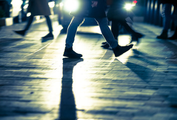 Backlit legs of people crossing the road against car at night