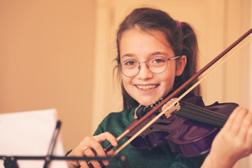 Cute child (little girl) playing violin and exercising at home