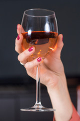 Kobieca dłoń z umalowanymi na czerwono paznokciami i obrączką ślubną na palcu trzyma kieliszek z winem.
