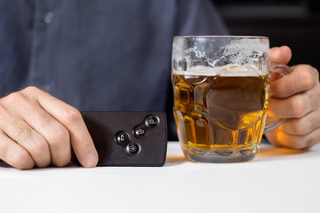 Dłonie mężczyzny w jednej ręce trzymają kartę kluczyk do samochodu, w drugiej kufel z piwem.