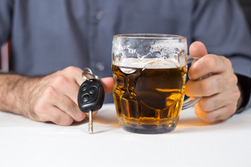 Na pierwszym planie kluczyki od samochodu trzymane w męskiej dłoni. W tle kufel z piwem. - obrazy, fototapety, plakaty