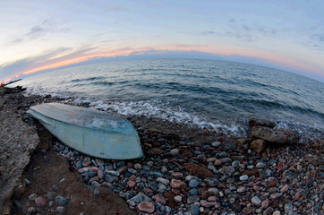 Old boat at Issyk-Kul lake shore, sunset landscape with beautiful stones and surf