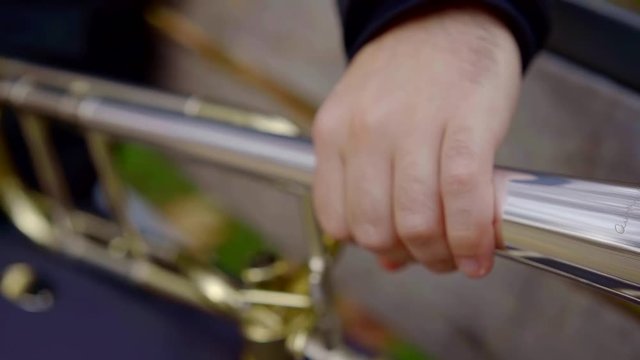Close-up shot of a musician taking his brass intrument and preparing to play song outdoor in park.