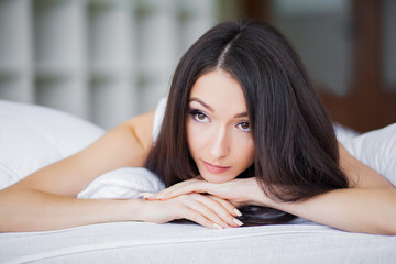 Good morning. Portrait of a smiling pretty young brunette woman relaxing in white bed