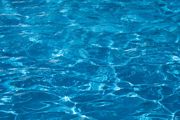 Blue and bright ripple water surface in swimming pool with sun reflection.