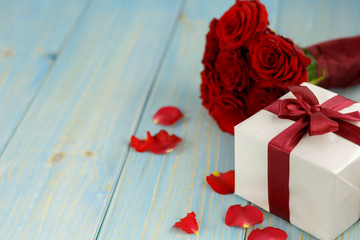 Red roses and gift box on light blue wooden table.