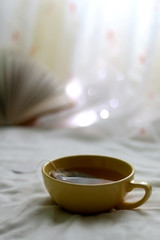 Cup of hot tea. Book and fairy lights in the background. Seletive focus.