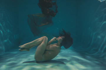 beautiful girl in a transparent jumpsuit with rhinestones on the whole body swims underwater as a...