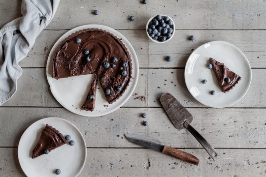 Dark chocolate tart with fresh blueberries served on a wooden rustic table 