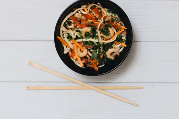 Chopsticks and delicious salad with vegetables shrimps in black plate, Asian cuisine