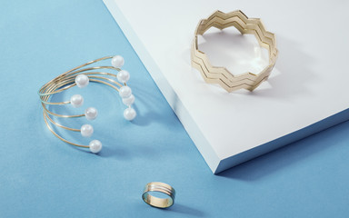 Shiny Golden bracelets and a ring on white corner on blue paper background