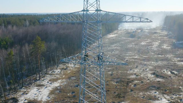 Aerial circling view of steel erector workers working on the just installed power line pylon (transmission or power tower)