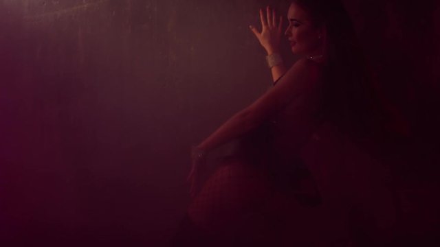 Hot woman shaking and waving her buttocks leaning on the wall, sexy dancer's costume of club girl. Stage gogo dancing in smoke. Shoot with RED RAVEN camera. 