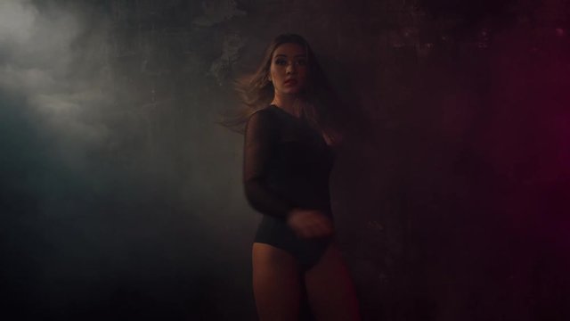 Sexy brunette girl in black dress dancing by the wall in beautifuly red lit room with smoke. Passionate young gogo dance, energetic lifestyle. Shoot with RED RAVEN camera. 