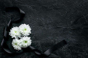 Funeral symbols. White flower near black ribbon on black background top view space for text - obrazy, fototapety, plakaty