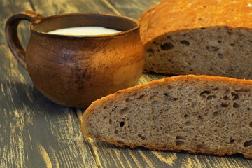 Home-made tasty soft fragrant ruddy rye bread and clay cup with milk on dark natural wooden background. Forgotten recipes. Selective focus.