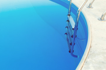 Close-up of a part of swimming pool with a stainless steel ladder and blue water on sunset. Summer vacation, holidays, relax, summer activities concept