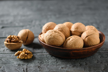 Split walnut with a clay bowl full of nuts on a dark rustic table.