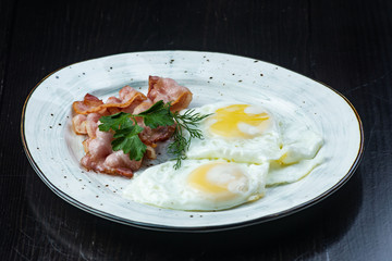 Scrambled eggs and bacon in a white plate on a dark background close-up. Omelet