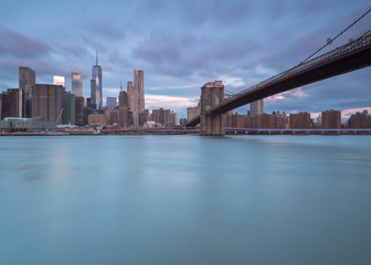 View on Brooklyn Bridge and financial district from east river at sunrise with long exposure