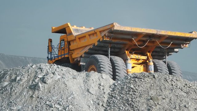 Heavy dump truck finishes to unload the ore and leaves the quarry. View from back.
