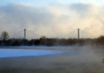 Pedestrian bridge in the city of Krasnoyarsk. Winter landscape. The ice on the river. The mist over the water. Low air temperature.