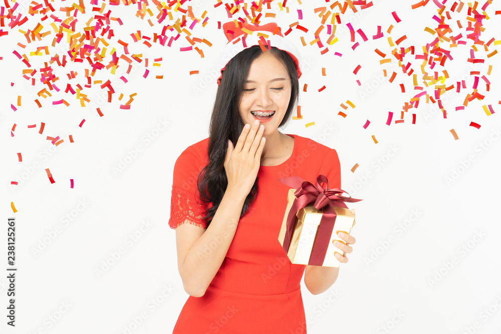 Wall mural Photo of asian curious woman in red dress rejoicing her birthday or new year gift box. Young woman holding gift  box with red bow being excited and surprised  holiday present isolated white background