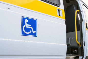 The open door of a specialized vehicle for people with disabilities. White bus with a blue sign for the disabled. Yellow bar and handrail.