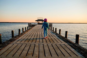 A little girl in a bicycle helmet on the pier seems nervous by the vast size of the Neuse River estuary at a park in Arapahoe North Carolina.