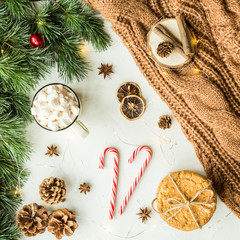 Christmas flatlay items. Cup of coffee with marshmallow, tree, brown sweater, garland lying on gray concrete background. Top view