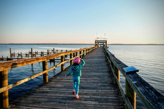 A little girl in a bicycle helmet runs on the pier at the Neuse River estuary at a park in Arapahoe North Carolina.