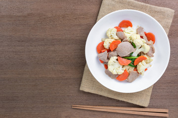 top view of stir fried cauliflower with pork in a ceramic plate on wooden table. homemade style healthy food concept.
