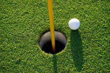Golf ball on the edge of hole on the green grass