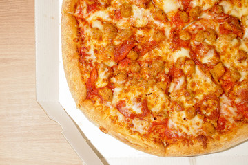 Pizza with Italian sausages and pepperoni in a white box, on a wooden table