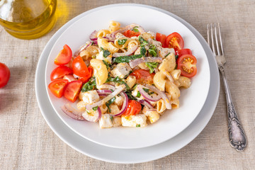 Warm pasta salad, cherry tomatoes, feta cheese and onions on a plate, top view, rustic background