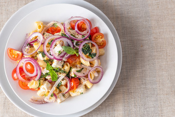 Warm pasta salad, cherry tomatoes, feta cheese and onions on a plate, top view, copy space for recipe, rustic background