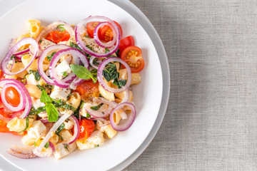Warm pasta salad, cherry tomatoes, feta cheese and onions on a plate, top view, copy space for recipe, rustic background