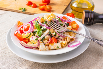 Warm pasta salad with cherry tomatoes, feta cheese and onions on a plate on the table