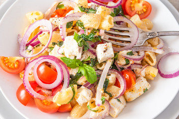 Warm salad of pasta, cherry tomatoes, feta cheese and onions on a plate, standing on the table, close-up