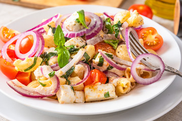 Warm salad of pasta, cherry tomatoes, feta cheese and onions on a plate, standing on the table, close-up