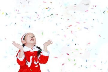 Happy child girl in Santa costume dress with colorful confetti ribbon paper thrown on white background. Merry Christmas and Happy New Year Concept.