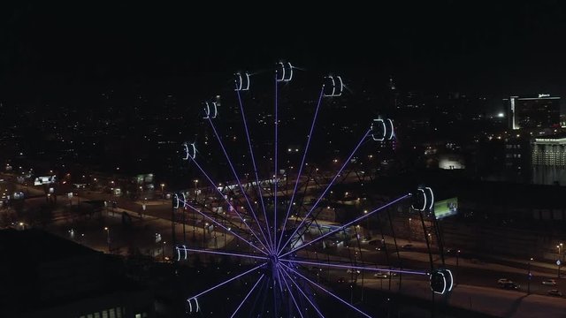 Aerial; drone flight down near the illuminated ferris wheel with night cityscape on background; Chelyabinsk, Russia