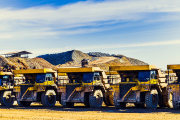 Big yellow dumpers put in a row in the mine with tipper laden with ore along the way