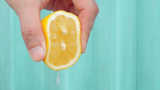 Scene of hand squeeze fresh lemon juice with blue background.