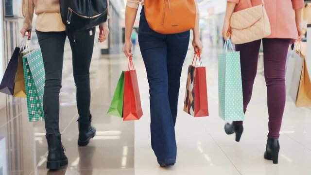 Low shot of female shoppers walking in shopping center together holding gift bags with purchases enjoying sale. People, consumerism and shopaholism concept.