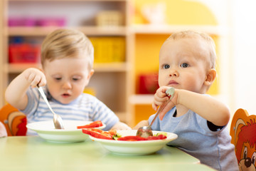 babies children boys eating healthy food in nursery or kindergarten