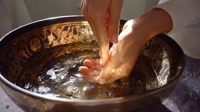 female hands are scooping water from beautiful traditional oriental bowl, washing and cleansing