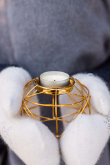 Golden metal candlestick in the hands of a woman in white mittens utdoor. Winter christmas mood