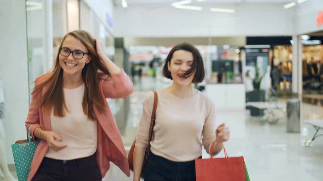 Attractive young women are walking in shopping center with bags, looking around, talking and laughing having fun enjoying new collection of clothing.